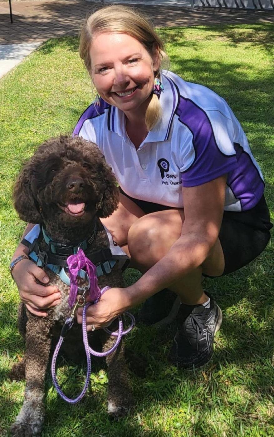 A volunteer kneeling with her poodle on the grass