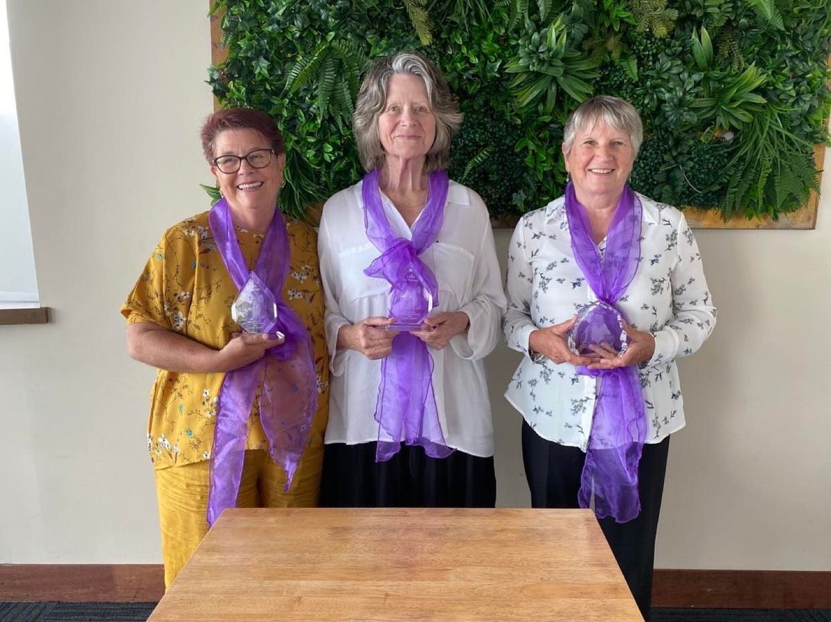 Three volunteers wearing sashes at a PAWS awards evening