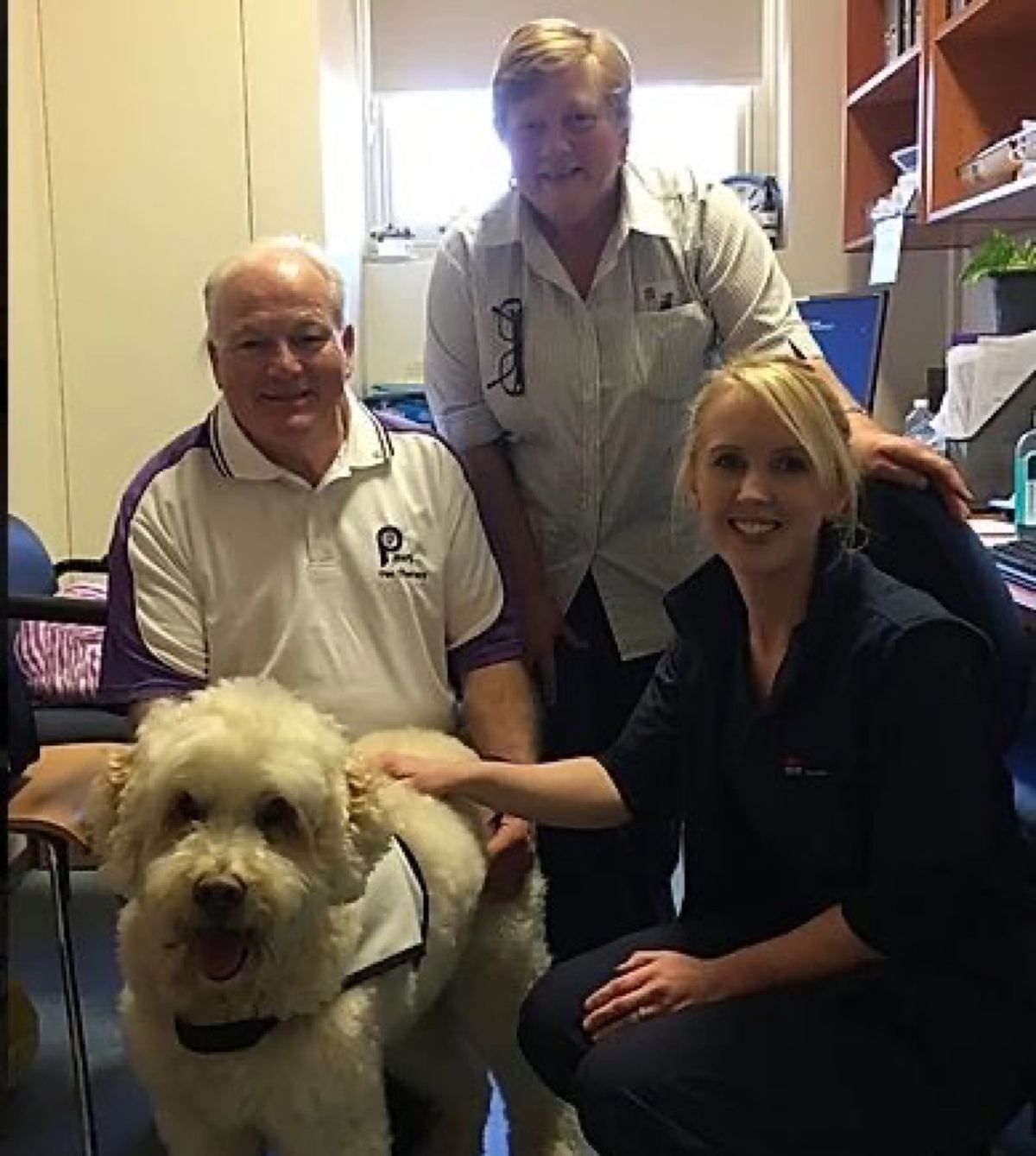 Two volunteers with their goldendoodle PAWS therapy dog outdoors