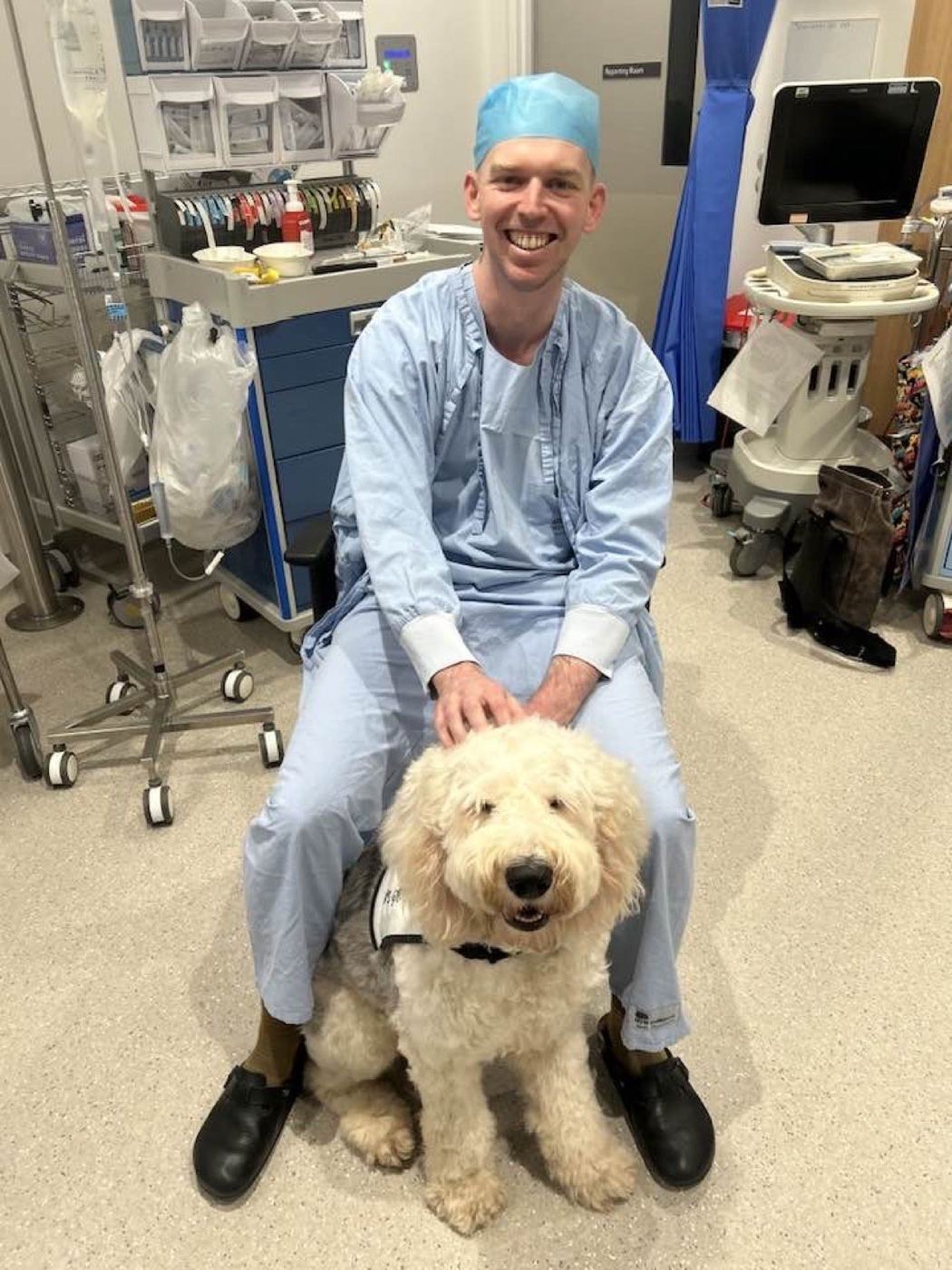 A patient in a hospital bed with a PAWS therapy dog resting beside him
