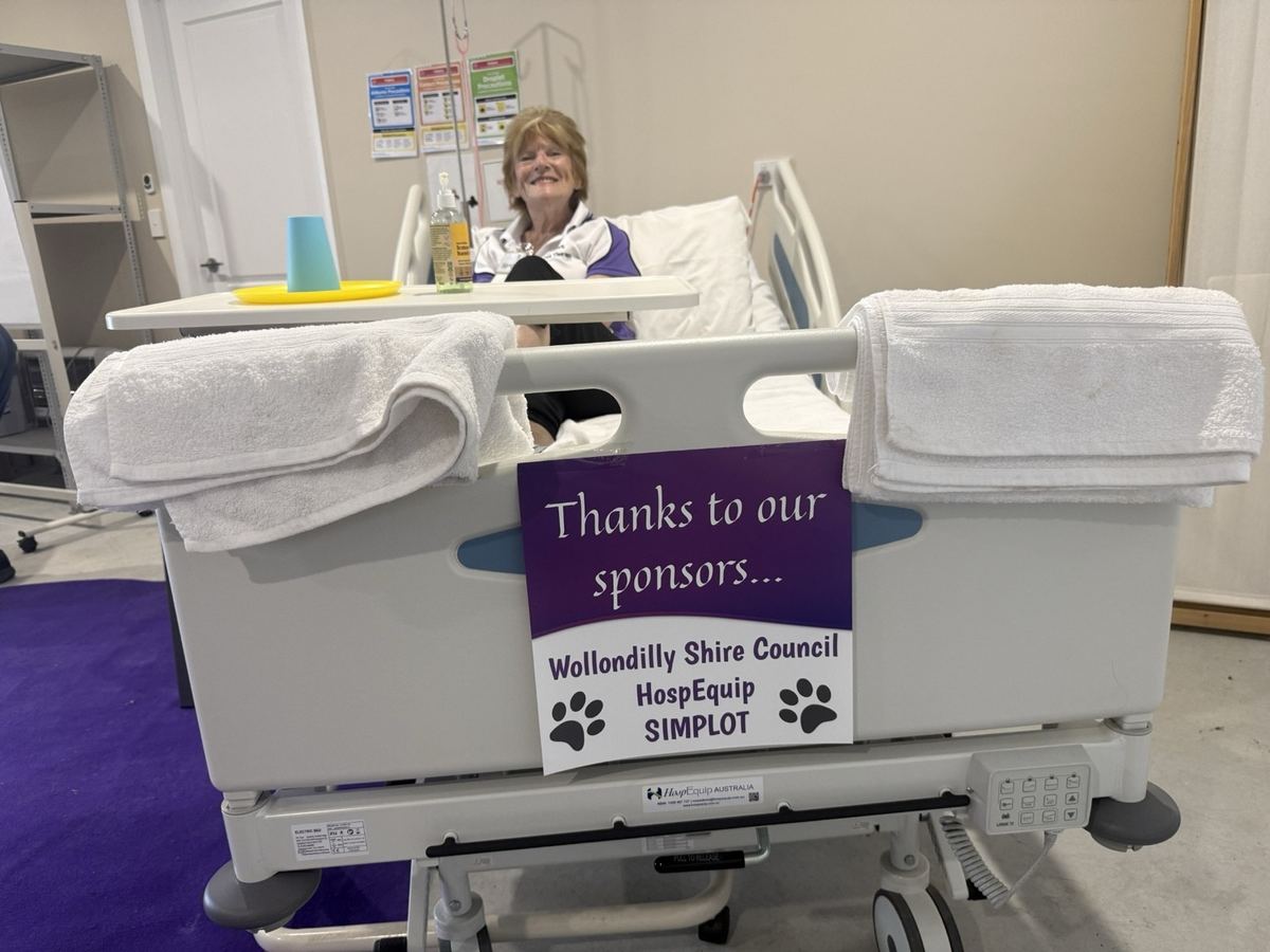 A 'Thanks to our sponsors' sign for Wollondilly Shire Council, HospEquip and Simplot on a hospital bed used for PAWS training