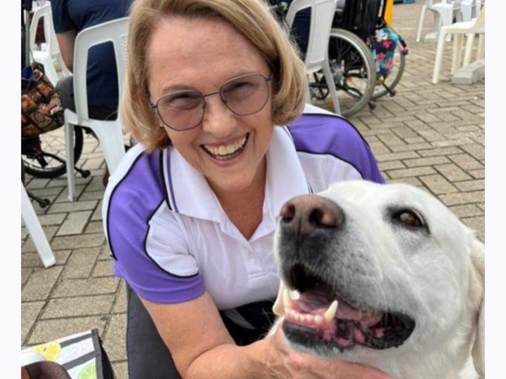 A smiling volunteer hugging her white labrador