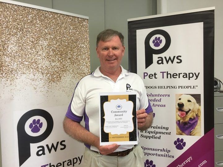 A volunteer holding a certificate beside a PAWS banner