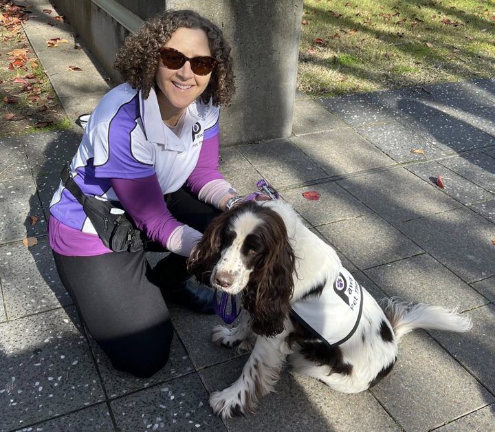 A volunteer in sunglasses kneeling beside her spaniel