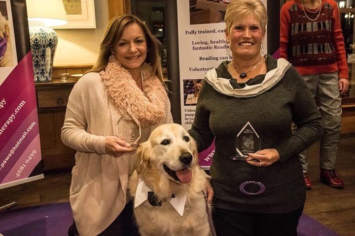 Two women with a golden retriever at a function