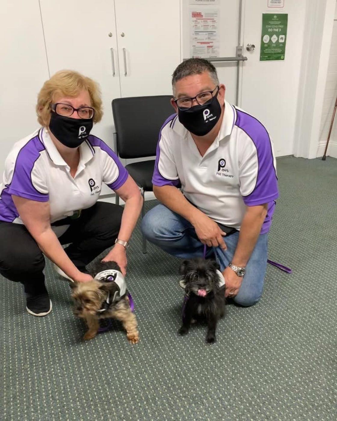 Two volunteers in masks kneeling with their small dogs