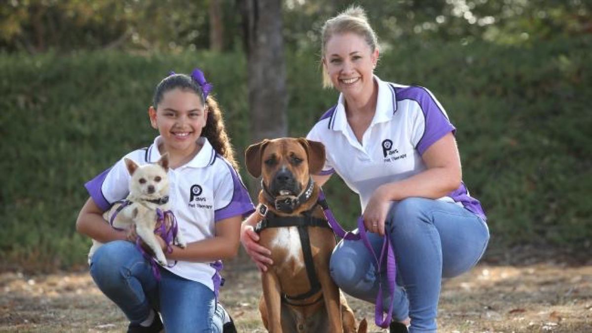 Two PAWS volunteers kneeling with their own dogs, smiling